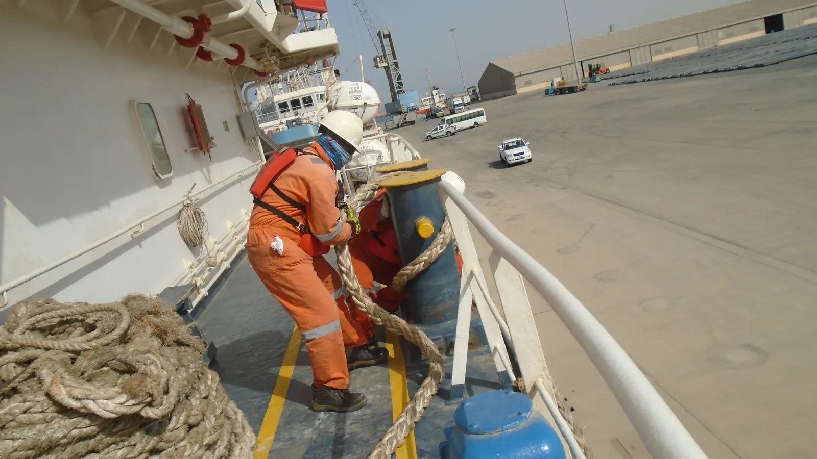 Ship mooring system with seafarers handling a mooring line on a merchant vessel